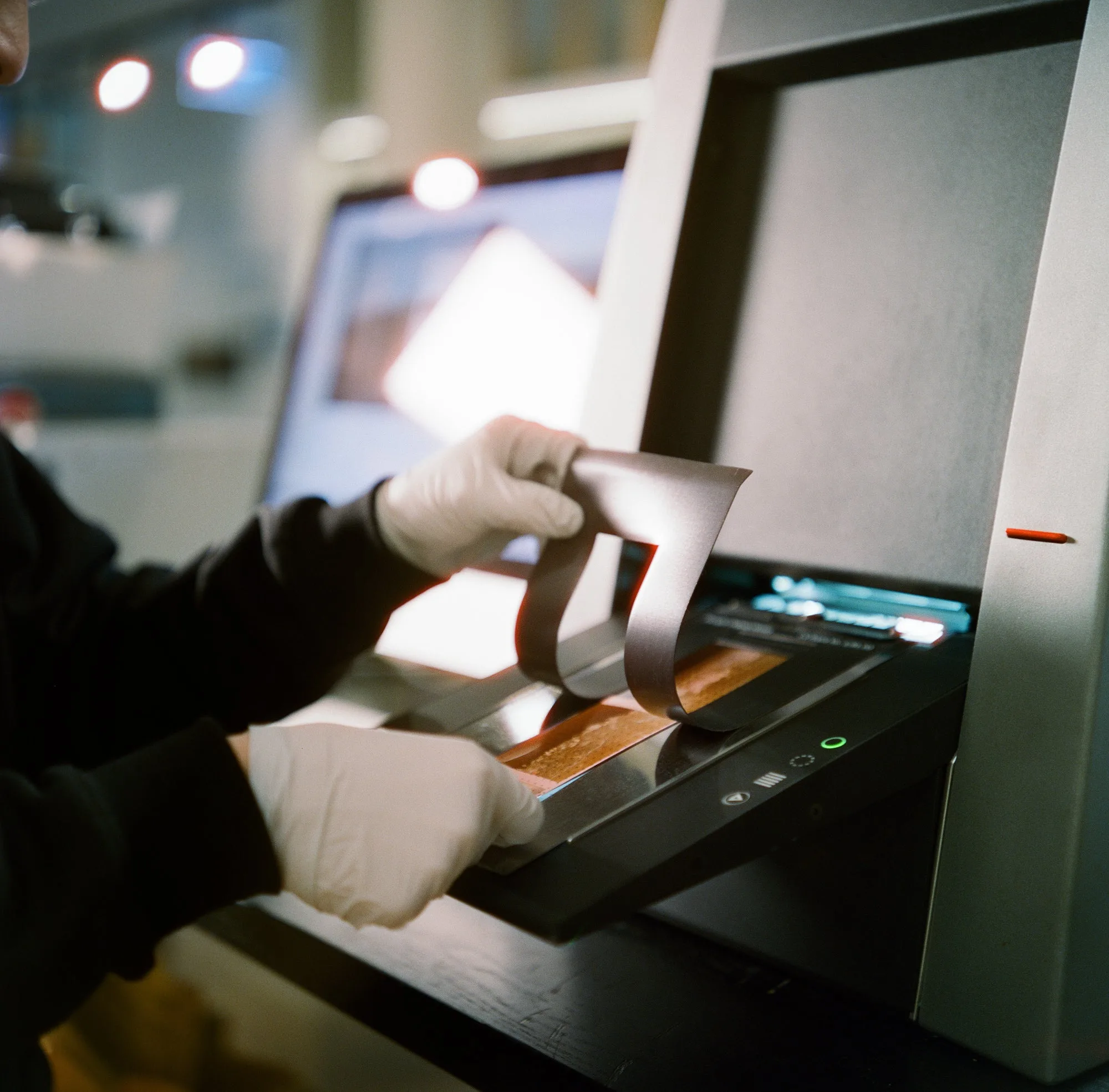 Gloved hands feeding a strip of colour negatives into a film scanner