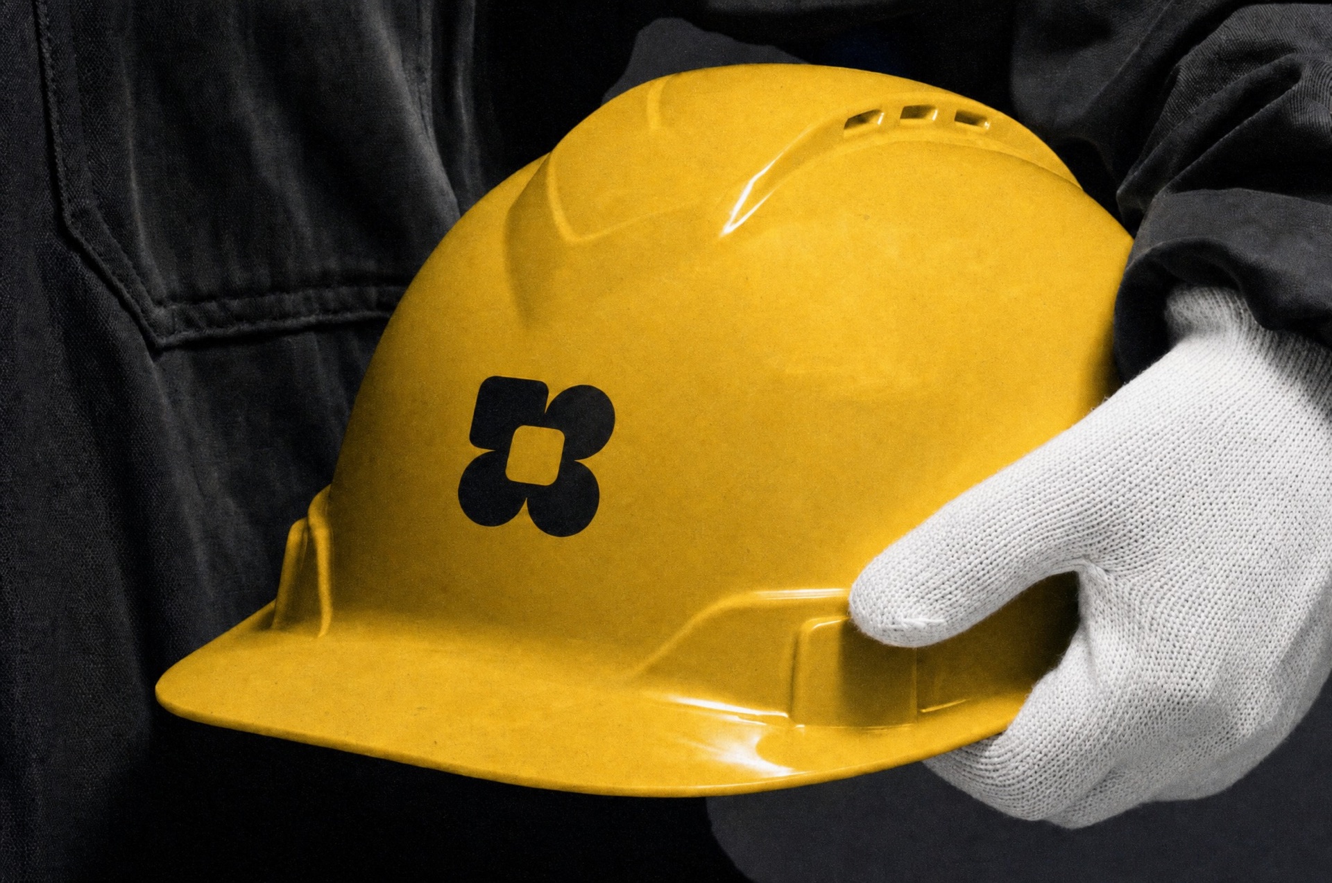 Yellow hard hat with the AirBuild mark, held in a work glove
